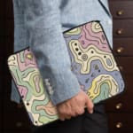 Laptop sleeve with topographic map design in pastel colors, featuring contour lines on a neutral background. the person holding the sleeve