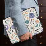 Organic abstract laptop sleeve with hand-drawn patterns in coral, purple, mint green, and black on a white background with a zip closure. The laptop sleeve covers the laptop