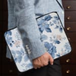 Laptop sleeve with a blue floral design, featuring light and dark blue flowers on a white background with a secure zip closure. the person holding the sleeve