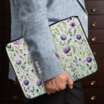 Laptop sleeve with purple floral design, featuring purple flowers and green leaves on a light background, with a secure zip closure. the person holding the sleeve