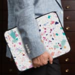 Laptop sleeve featuring a pastel terrazzo design with irregular shapes in pink, blue, turquoise, and dark shades on a light background. the person holding the sleeve