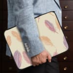 Infidu Pastel Feather Laptop Sleeve with a soft feather design in pastel shades on a light background, displayed on a white desk. the person holding the sleeve