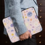 Laptop sleeve with a playful, abstract design featuring colorful shapes like swirls, circles, and dots on a white background. the person holding the sleeve