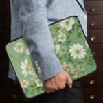 Floral laptop sleeve with white flowers and green leaves on a soft green background. the person holding the sleeve