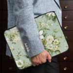 Floral laptop sleeve with white flowers and green leaves on a soft green background. the person holding the sleeve