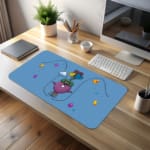 Infidu Cartoon Bird Desk Pad featuring a purple bird with glasses and a green hat, surrounded by colorful balloons and hearts on a light blue background. desk pad kept on the table