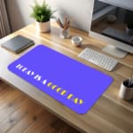 Infidu Today Is A Good Day Design Desk Pad featuring yellow and white text on a light blue background, perfect for inspiring workspaces. A desk pad under the computer