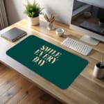 Infidu Smile Everyday Design Desk Pad featuring bold white text on a dark green background, perfect for uplifting workspaces. desk pad kept on the table