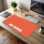 Infidu Be Kind Design Desk Pad featuring bold white text on a bright orange background, perfect for promoting kindness in your workspace. desk pad kept on the table