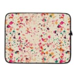 Laptop sleeve with a colorful terrazzo pattern in pink, orange, yellow, green, and black shapes on a white background, with a zip closure. laptop sleeve kept on a plain white background