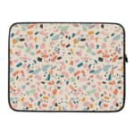 Terrazzo design laptop sleeve with blue, brown, and beige shapes on a light background, placed on a white desk with office supplies. laptop sleeve kept on a plain white background