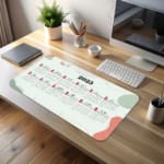 Infidu Calendar Design Desk Pad displaying a 2025 calendar layout with a light background and abstract red and gray accents. desk pad kept on the table