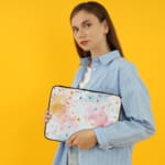 Colorful splatter paint design laptop sleeve with blue, orange, and pink splashes on a light background. the person holding the sleeve