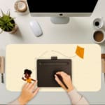 Infidu desk pad featuring a child flying an orange kite against a light sandal background. A computer and laptop are next to the desk pad