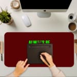 Infidu Always Be Kind To Yourself Desk Pad featuring bright green text on a maroon background, perfect for promoting self-care at your desk. A writing pad on top of the desk pad