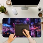 Infidu Neon City Street Desk Pad featuring a rainy night cityscape with people holding umbrellas, neon lights, and reflective wet streets. A computer and laptop are next to the desk pad