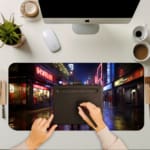 Infidu Neon City Street Design Desk Pad with a lively urban night scene, featuring neon reflections on wet pavement and silhouetted city figures. A desk pad under the computer