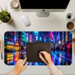 Infidu Neon City Street Desk Pad features a vibrant nighttime city scene with neon lights reflecting on a wet street, perfect for an energetic workspace. A writing pad on top of the desk pad