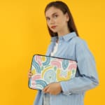 A colorful abstract laptop sleeve featuring pastel pink, blue, yellow, and green curved shapes on a white background with a zip closure. laptop sleeve kept on a plain white background the person holding the sleeve