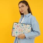 Laptop sleeve with a pastel bubble pattern in light blue, coral pink, and peach circles on a white background, secured with a zip closure. the person holding the sleeve