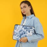 Laptop sleeve with a blue floral design, featuring light and dark blue flowers on a white background with a secure zip closure. the person holding the sleeve