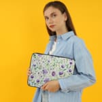 Laptop sleeve with purple floral design, featuring purple flowers and green leaves on a light background, with a secure zip closure. the person holding the sleeve