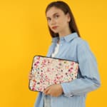 Laptop sleeve with a colorful terrazzo pattern in pink, orange, yellow, green, and black shapes on a white background, with a zip closure. the person holding the sleeve