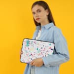 Laptop sleeve featuring a pastel terrazzo design with irregular shapes in pink, blue, turquoise, and dark shades on a light background. the person holding the sleeve