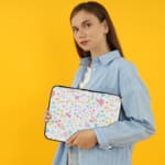 Laptop sleeve with colorful polka dots in pastel shades of pink, blue, yellow, and purple on a light background, with a secure zip closure. the person holding the sleeve