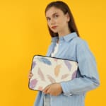 Laptop sleeve with a soft pastel feather design in pink, blue, purple, and orange on a light background, featuring a secure zip closure. the person holding the sleeve