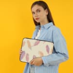 Infidu Pastel Feather Laptop Sleeve with a soft feather design in pastel shades on a light background, displayed on a white desk. the person holding the sleeve