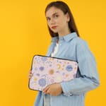 Laptop sleeve with a playful, abstract design featuring colorful shapes like swirls, circles, and dots on a white background. the person holding the sleeve