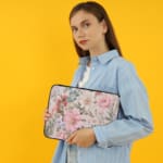 Laptop sleeve with a pastel floral design in pink, blue, and green on a white background, creating an elegant, gentle look. the person holding the sleeve the person holding the sleeve