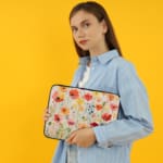 Colorful floral laptop sleeve with red, pink, yellow, and orange flowers on a light background. the person holding the sleeve