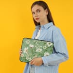 Floral laptop sleeve with white flowers and green leaves on a soft green background. the person holding the sleeve