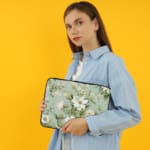 Floral laptop sleeve with white flowers and green leaves on a soft green background. the person holding the sleeve