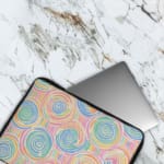 Laptop sleeve with a playful pastel spiral design on a white background. The laptop sleeve covers the laptop