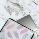 Infidu Pastel Feather Laptop Sleeve with soft fabric in pink, blue, and purple shades, featuring a zip closure for secure laptop protection. The laptop sleeve covers the laptop