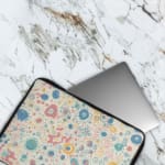 Laptop sleeve with a pastel bubble pattern in light blue, coral pink, and peach circles on a white background, secured with a zip closure. The laptop sleeve covers the laptop