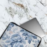 Laptop sleeve with a blue floral design, featuring light and dark blue flowers on a white background with a secure zip closure. The laptop sleeve covers the laptop