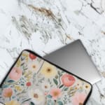 Infidu Vibrant Floral Laptop Sleeve with red, yellow, pink, and white flowers against a light background on a white desk.