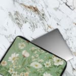 Floral laptop sleeve with white flowers and green leaves on a soft green background. The laptop sleeve covers the laptop